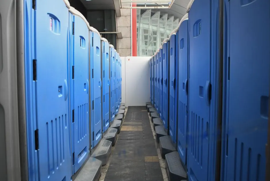 A series of blue portable toilets aligned at an outdoor construction site.
