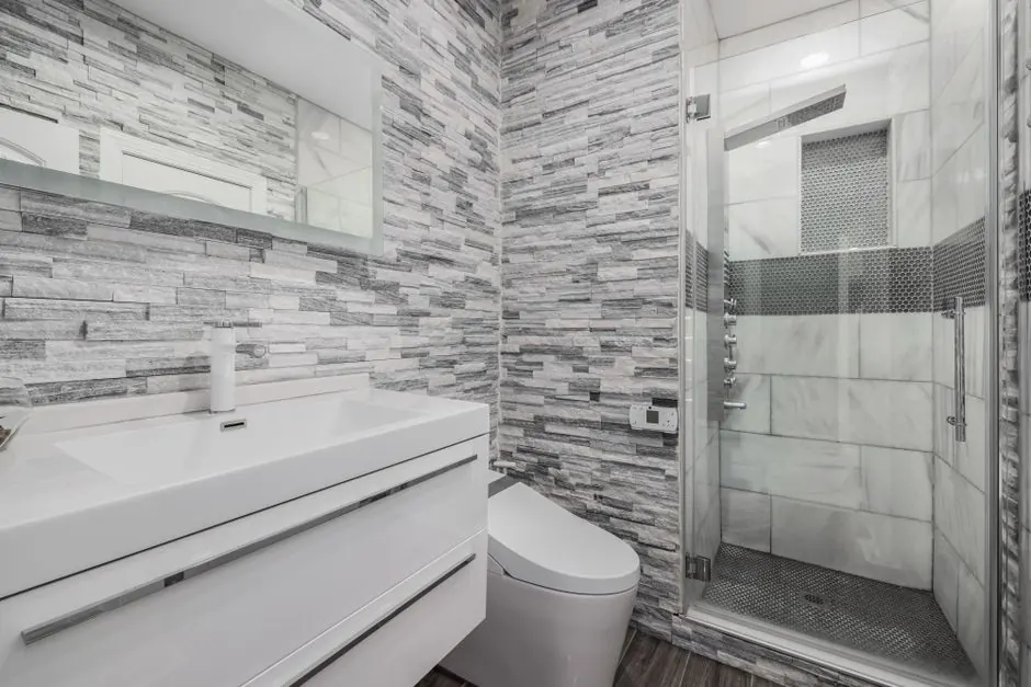 Stylish modern bathroom featuring a glass shower, stone walls, and sleek white vanity.